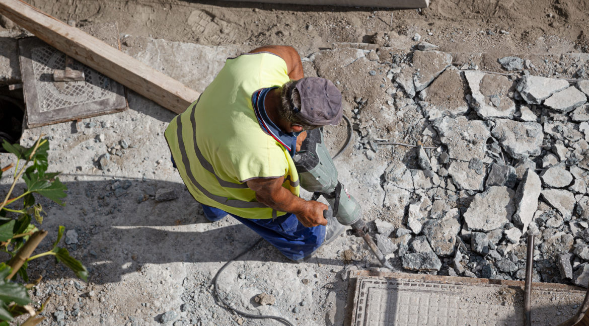 Construction worker with jackhammer drilling concrete on sidewalk. City Maintenance concept
