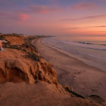Stunning sunset view from a cliff overlooking a Southern California beach, showcasing the coastal lifestyle of Ventura and Los Angeles Counties, perfect for real estate in 2025 buyer’s market, with a person relaxing.