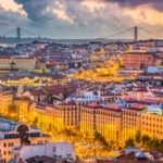 Panoramic view of Lisbon, Portugal, featuring yellow trams, cobblestone streets, and the Tagus River with Belém Tower, ideal for older adults seeking a simplified lifestyle after downsizing to this secure retirement haven. Shoket Properties.